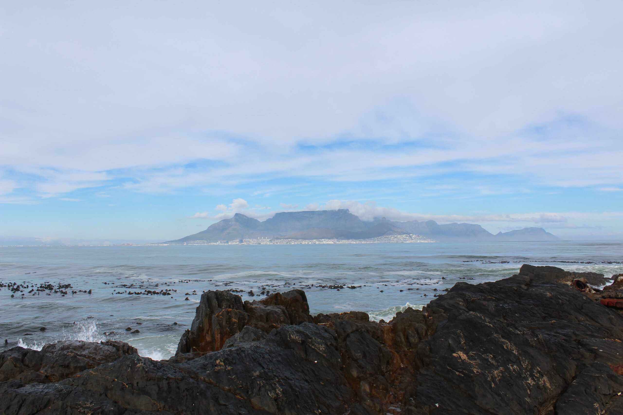 looking across a rocky sea to the hazy outline of a flat top mountain